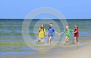 Two girls and two boys in colorful t-shirts running on sandy beach