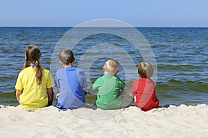 Two girls and two boys in colorful t-shirts sitting on a sandy beach