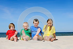Two girls and two boys in colorful t-shirts sitting on a sandy beach