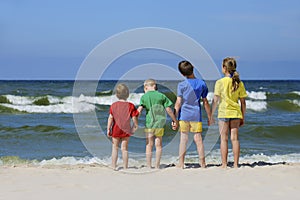 Two girls and two boys in colorful t-shirts standing back on a sandy beach