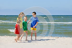 Two girls and two boys in colorful t-shirts walking on a sandy beach