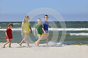 Two girls and two boys in colorful t-shirts walking on a sandy beach