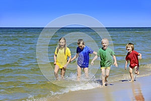 Two girls and two boys in colorful t-shirts walking on a sandy beach