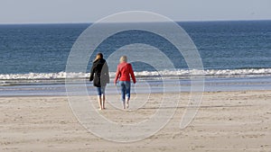 Two girls walk along the sandy beach in Northern Ireland on a chilly day in autumn