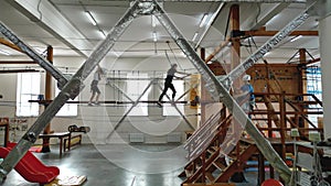 Two girls walk along a thin rope in a rope park indoors in protective gear