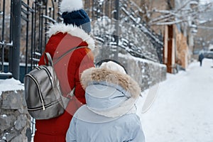 Two girls walking along the winter snowy street of the city, children are holding hands, back view