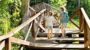 Two girls are walking on a hiking trail with a backpack to a family camp on sunny day. Beautiful wooden road in the forest for