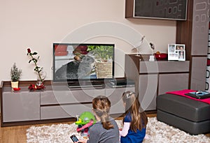 Two girls watching television at home, sitting on the carpet, nature programme photo