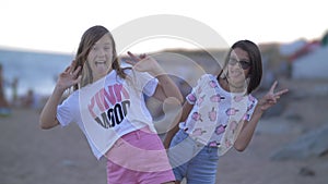 Two girls waving hands on beach in the evening, fooling at the camera, summer vacation, gesture
