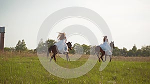 Two girls in white dresses on horseback. Girls jumping on the field on horseback. Slow motion.