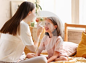 Two girls, younger and older happy sisters enjoying time together, playing and having fun while sitting on the bed in pajamas