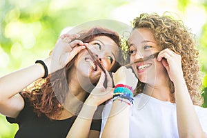 Two girs making moustache with their hair.