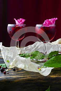 Two glases full of red drink with berries, ice and a pink flower