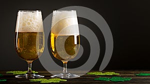 Two Glass of Beer or Ale on wooden table and clover leaves on black background. St. Patrick`s Day.