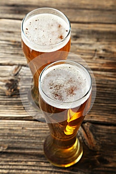 Two glass of beer on brown wooden background.