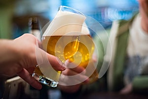 Two glass of beer in hand. Beer glasses clinking in bar or pub