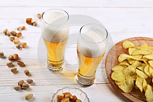 Two glass of beer and snacks on a white wooden table. Chips, pistachios, dry cheese.