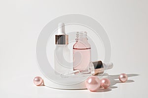 Two glass bottles of cosmetic liquid transparent gel on white background with pink pearls. Dropper bottle, hyaluronic