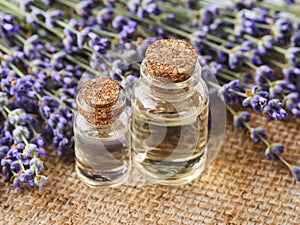 Two glass bottles of lavender essential oil and fresh fragrant lavender on a jute sackcloth background. Spa, beauty, skin care and