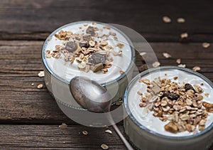 Two glass bowls with white yogurt on old wooden desk with oatmeal on top