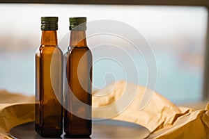 Two glass brown transparent faceted bottles empty and full with vegetable oil with green caps stands on a black plate on paper.