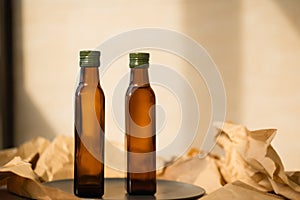 Two glass brown transparent faceted bottles empty and full with vegetable oil stands on a black plate on paper. Salad dressing.