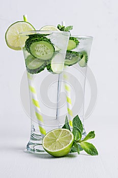 Two glass with cold detox water with slices cucumber, lime, mint, ice, straw on white wood plank.