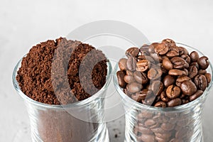 Two glass cups with coffee beans and ground coffee on light concrete background