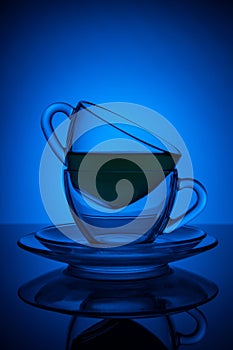 Two glass cups with tea and saucer with reflection, on a blue and black gradient background. Concept, party and club