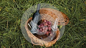 Two glass of empty wine with bottle with red wine in wicker picnic basket outdoors. Summer romantic lunch