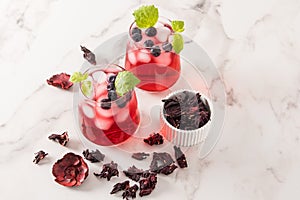 Two glass glasses with cold hibiscus tea, blueberries, lime slices and ice cubes on a marble table. high content of vitamins,