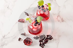 Two glass glasses with cold hibiscus tea, blueberries, lime slices and ice cubes on a marble table. high content of vitamins,