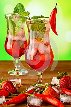 Two glass glasses with grenadine cocktail decorated with pepper and mint on a wooden table