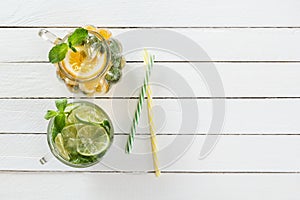 Two glass glasses with homemade lemonade from lime and lemon, cocktail tubes on a white wooden rustic background