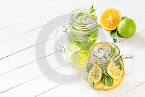 Two glass glasses with homemade lemonade from lime and lemon, sliced citrus on a white wooden rustic background