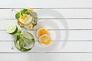 Two glass glasses with homemade lemonade from lime and lemon, sliced citrus on a white wooden rustic background