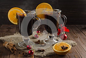 Two glass glasses of mulled red wine with orange slices stand on a dark wooden table.