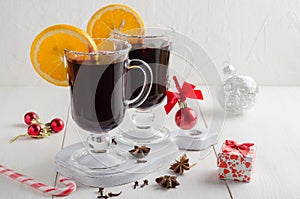 Two glass glasses of mulled red wine with orange slices stand on a white wooden table.