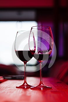 Two glass glasses with red wine inside against the light on a wooden table, indoors