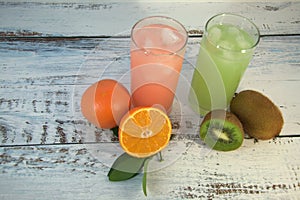 Two glass glasses with a refreshing juice and ice, on a textile stand, whole and sliced half of an orange with leaves and fruit,