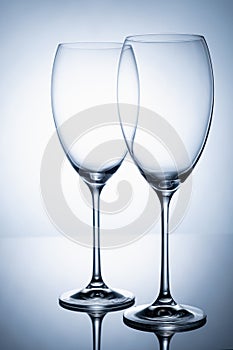 Two glass goblet without wine on a thin leg stands on a mirror surface