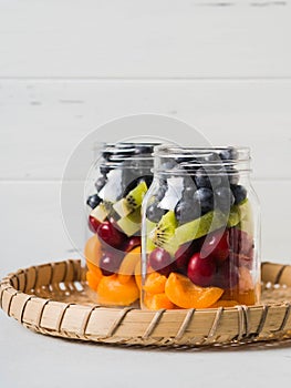 Two glass jars with berries and fruits. Fruit salad with apricots, kiwi, cherries and blueberries in glass jars on white