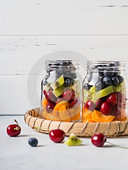 Two glass jars with berries and fruits. Fruit salad with apricots, kiwi, cherries and blueberries in glass jars on white