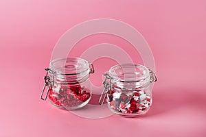 Two Glass Jars with Candy Sprinkles in Shape of Hearts and Lips on Pink Background Horizontal