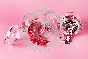 Two Glass Jars with Candy Sprinkles in Shape of Hearts and Lips on Pink Background Horizontal