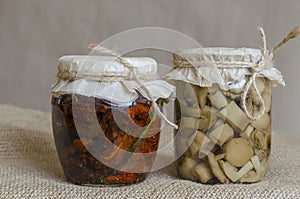 Two glass jars with canned mushrooms and sun-dried tomatoes