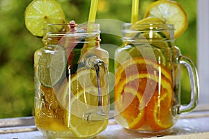 Two glass jars of cold, vitamin drink with sliced citrus fruits close-up.