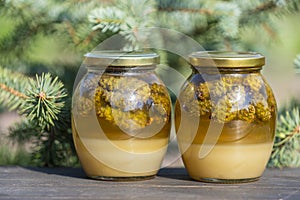 Two glass jars of fresh honey with pine cones on a wooden table, closeup