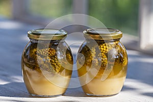 Two glass jars of fresh honey with pine cones on a wooden table, closeup