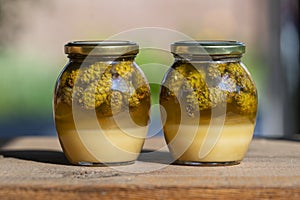 Two glass jars of fresh honey with pine cones on a wooden table, closeup